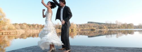 Tanzpaar im Balloutfit auf einem Steg am See. Sie dreht unter seinem rechten Arm, der Rock und die Haare fliegen durch die Drehbewegung. Beide lachen